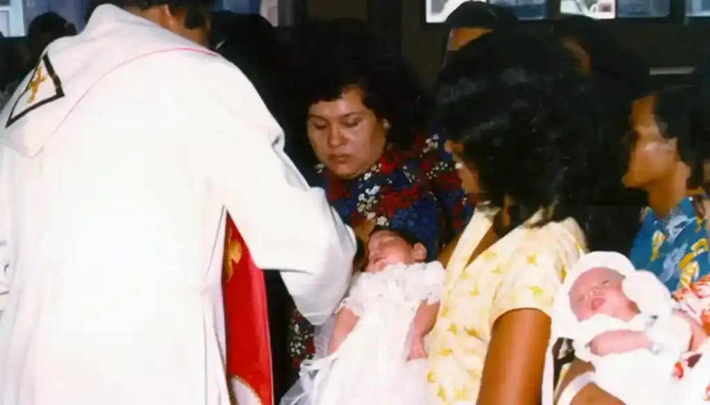 Godmothers, or ninas, watch as a priest anoints their godson with oil as part of the baotismo (baptism) ceremony in this 1980 photo at Santa Barbara Church in Dededo.