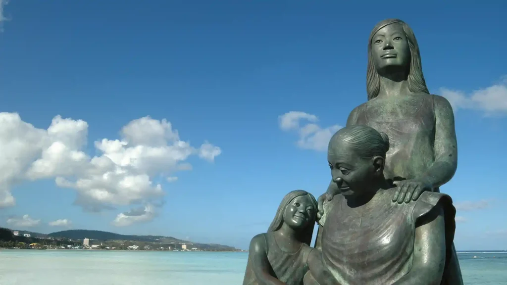Bronze statue of a mother with two children by the seaside under a blue sky.