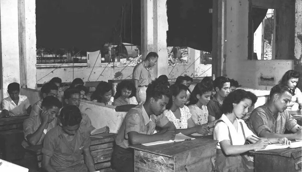 8 June 1945 Teacher Gus Duenas instructing a class in Social Science in bomb-shattered building. Micronesian Area Research Center (MARC) collection.