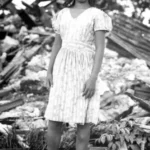 Beatrice Peredo Flores Emsley stands in the debris left over from World War II battles to recapture Guam by US Marines, 1944. Emsley was an influential voice for fellow Chamorro World War II survivors because of her powerful testimonies for War Reparations in the late 1980s and early 1990s.
