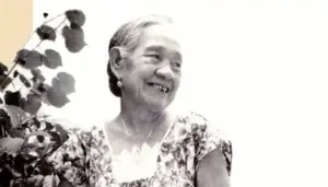 Master Suruhåna Angela Santos Palacios - Guampedia - Guampedia Older woman smiling, wearing a floral dress, with leaves in the foreground in a black-and-white photo